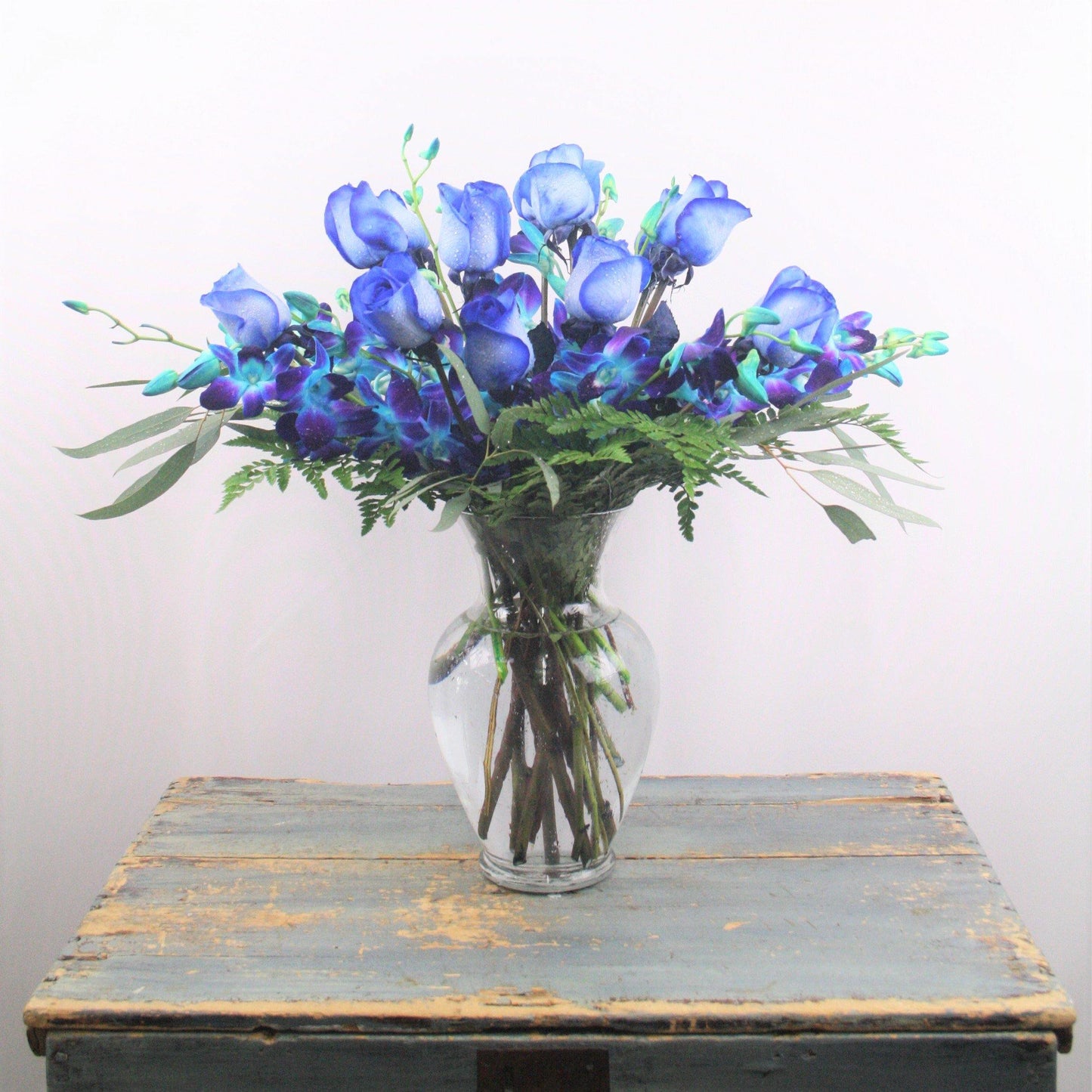 Bouquet with one dozen blue roses and blue dendrobium orchids in a large clear glass vase