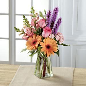 Bouquet with peach gerbera daisies, pink roses, snapdragons, mini carnations, purple liatris, and greenery in clear glass vase