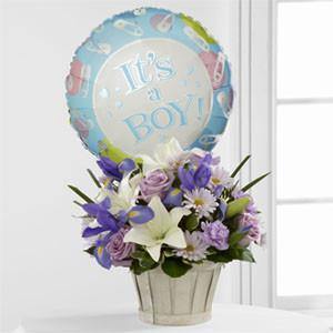 Bouquet with lavender roses, blue iris, lilies, carnations, daisies, and It’s a Boy balloon in white woodchip basket.