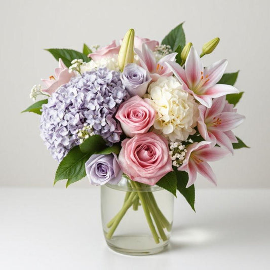 Bouquet of pink and lavender roses, pink lilies, and white and lavender hydrangeas in a clear glass vase