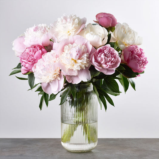 Bouquet of pink and white flowers in a clear vase on a wooden surface with a light gray background