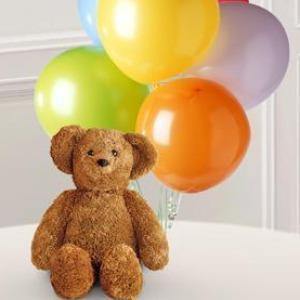 A plush bear holding six colorful latex balloons tied with a ribbon, perfect for birthdays, get well, or baby gifts.