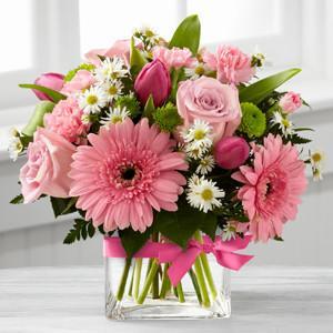 A pastel bouquet of pink roses, gerbera daisies, and carnations in a square glass vase with a satin ribbon.