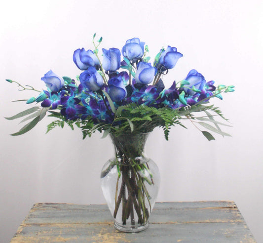 Bouquet with one dozen blue roses and blue dendrobium orchids in a large clear glass vase
