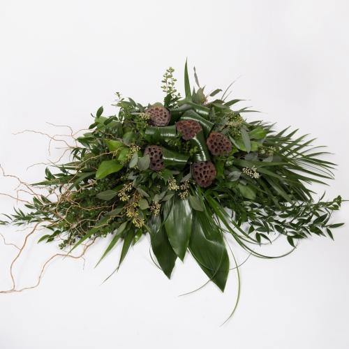 Casket spray with assorted greenery including aspidistra, lotus pods, curly willow, eucalyptus, ruscus, and palm greens