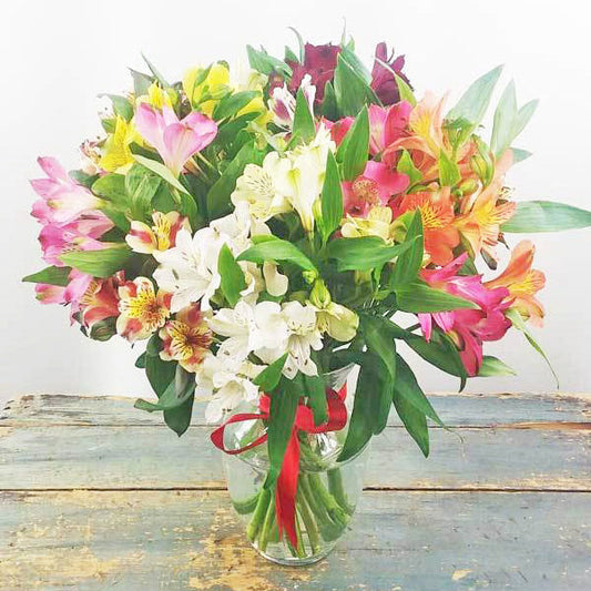 A cheerful bouquet of alstroemerias and greenery in a clear glass vase, perfect for any occasion.