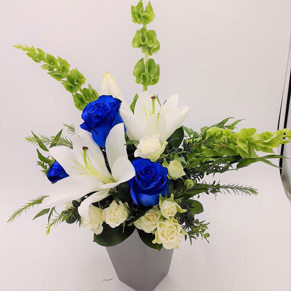 Man of Steel Bouquet featuring blue roses, white lilies, spray roses & Bells of Ireland arranged with greens in a vase 