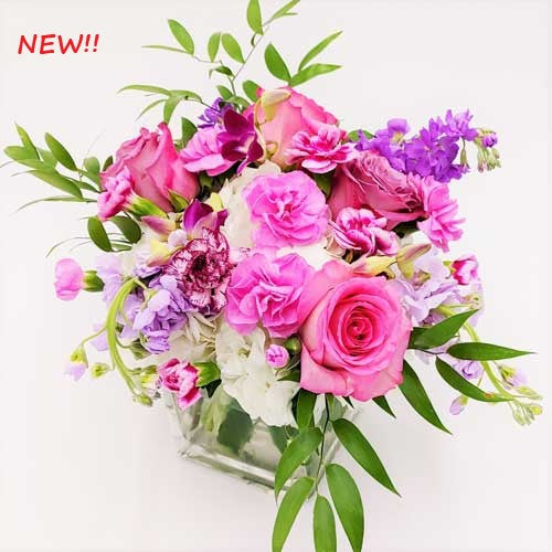 A bouquet of pink and purple flowers in a square glass vase, designed for celebrations.