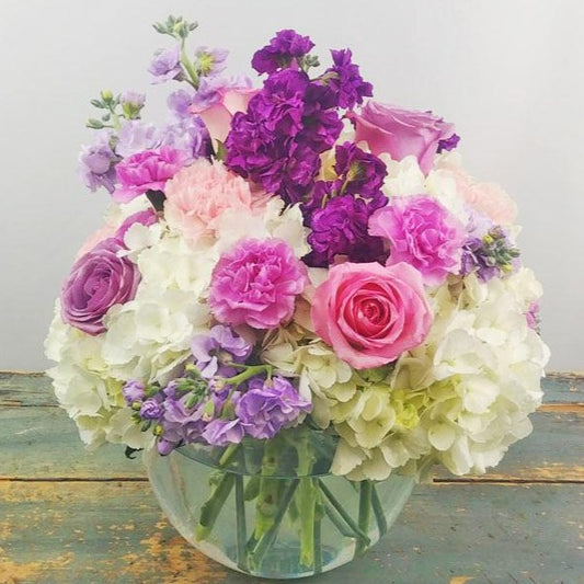 A pastel bouquet of pink roses, hydrangea, and lavender stock, accented with greenery, arranged for any special occasion.