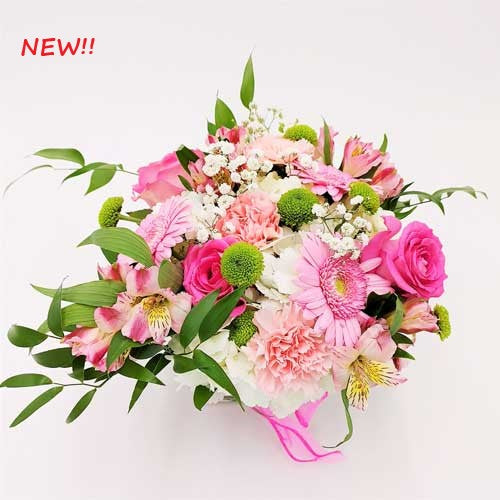 A bouquet of pink roses, gerbera daisies, hydrangea, and carnations in a clear square vase.