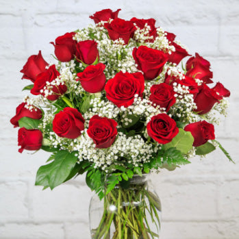 A luxurious bouquet of 24 long-stemmed red roses arranged in a classic glass vase.